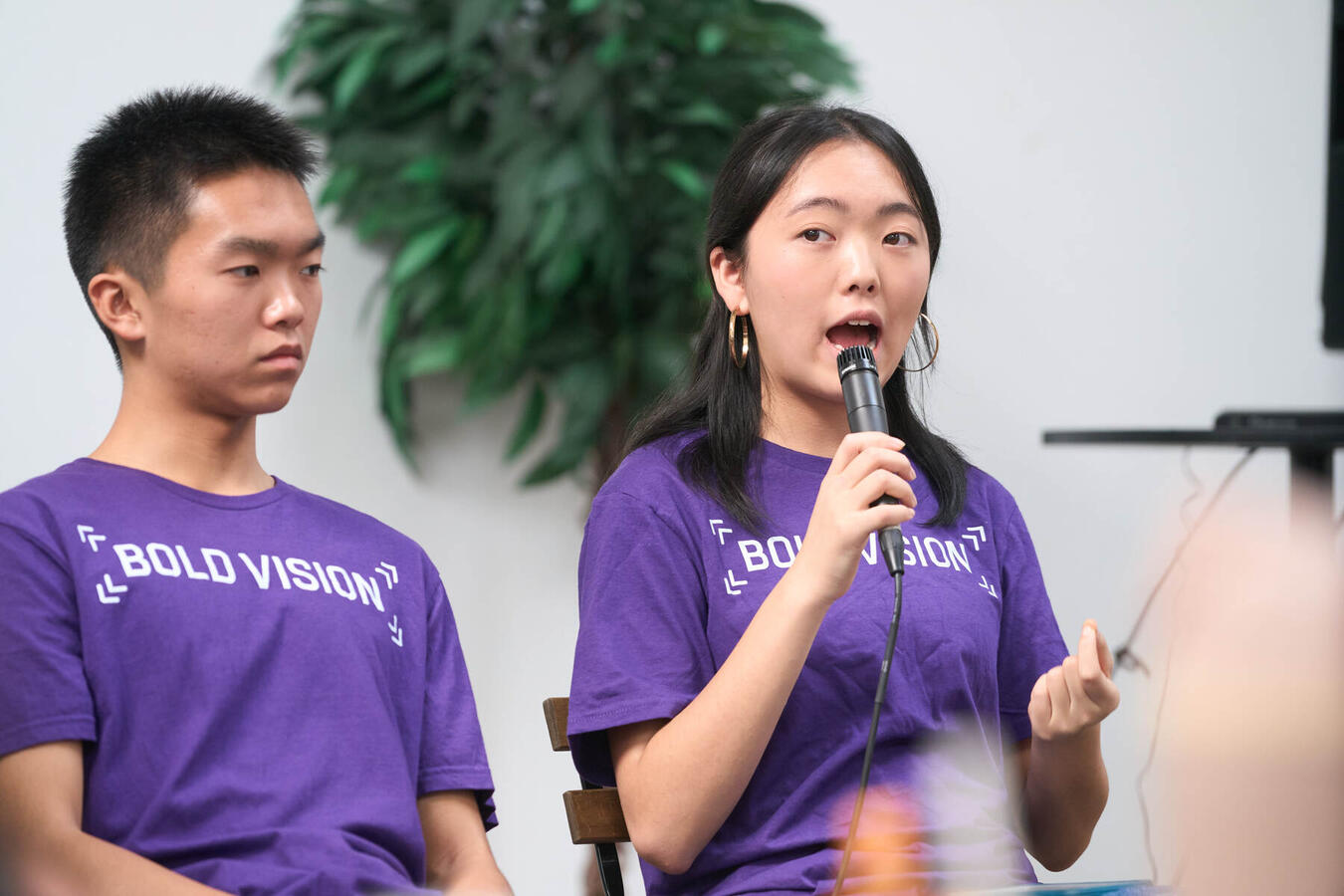 Two Bold Vision Youth Council members speak into a microphone during a summit presentation.