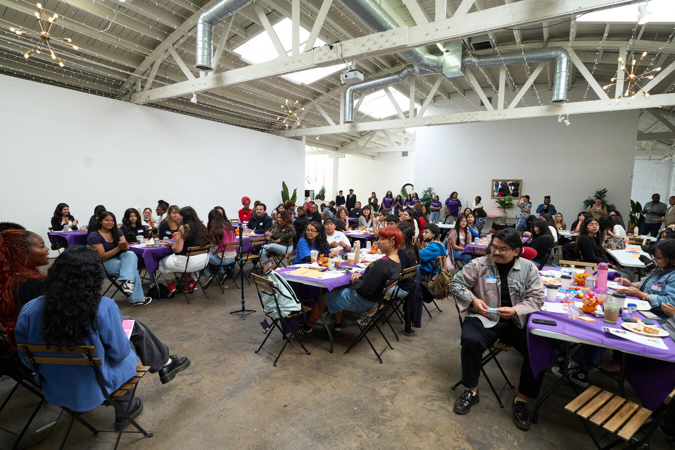Attendees Seated for the October Summit Attendees fill round tables inside a warehouse-style venue for the October Youth Summit.