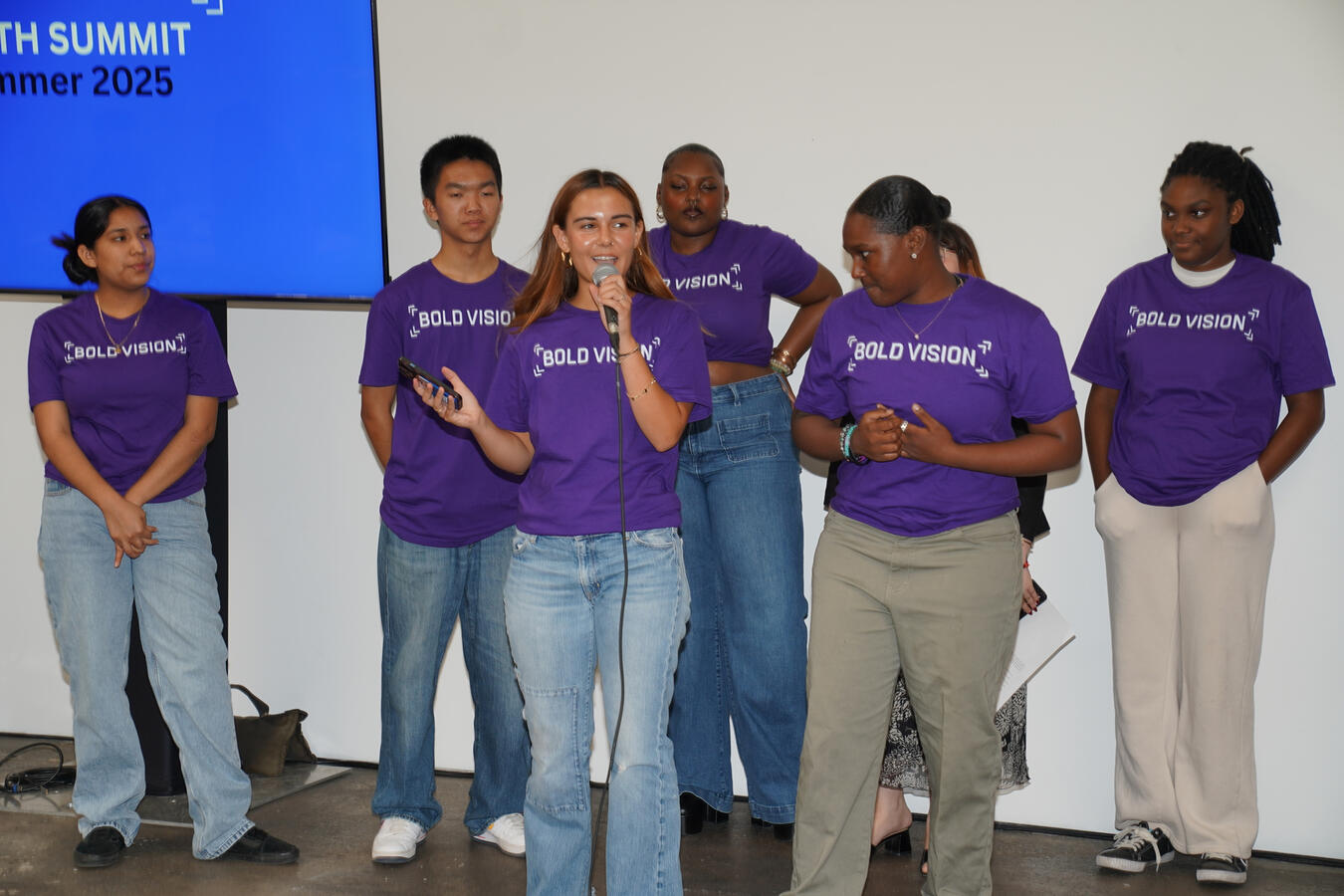 Bold Vision Youth Council members stand together on stage in purple shirts during the summit.