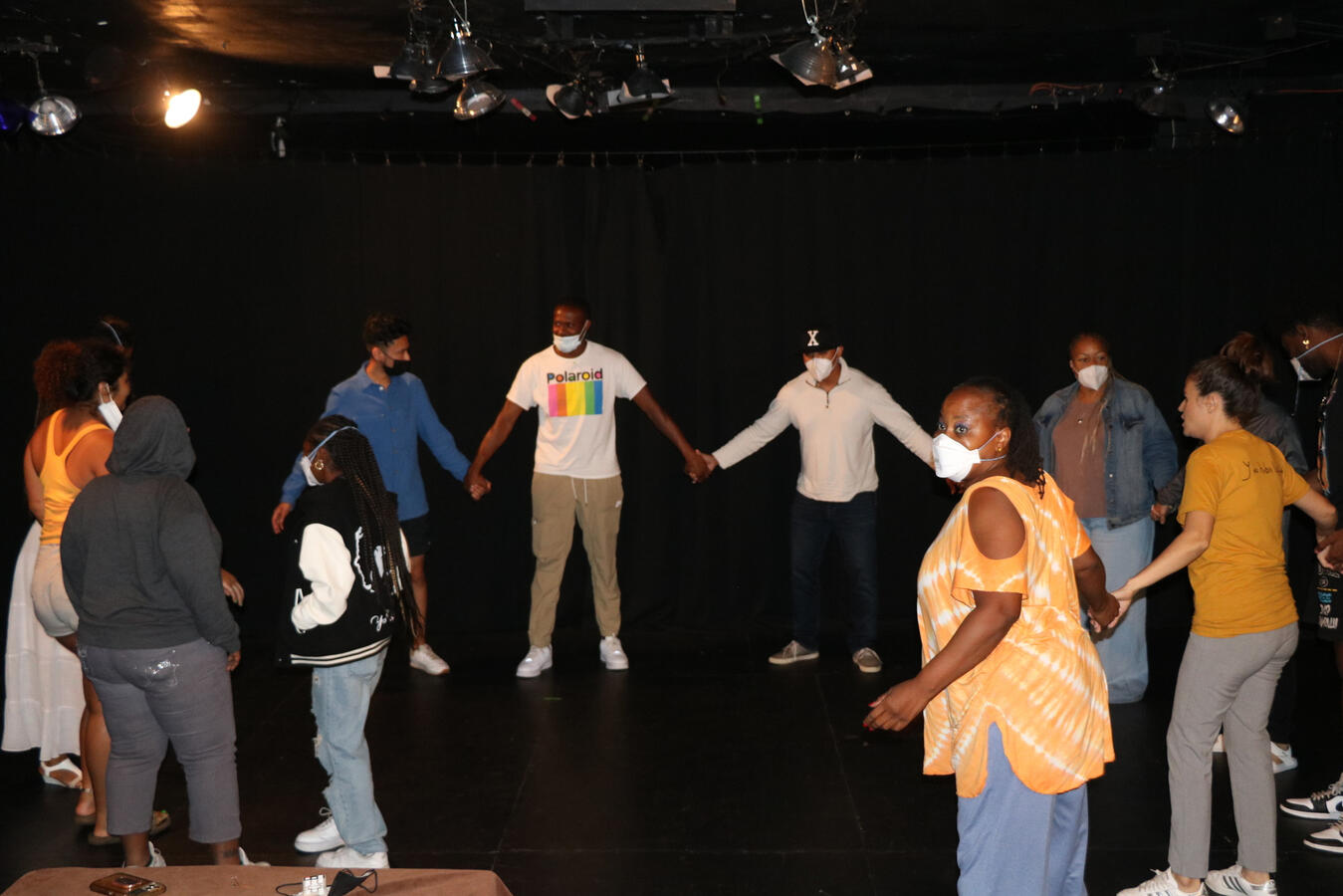 Delegation members hold hands in a circle on a dimly lit stage during a theater exercise.
