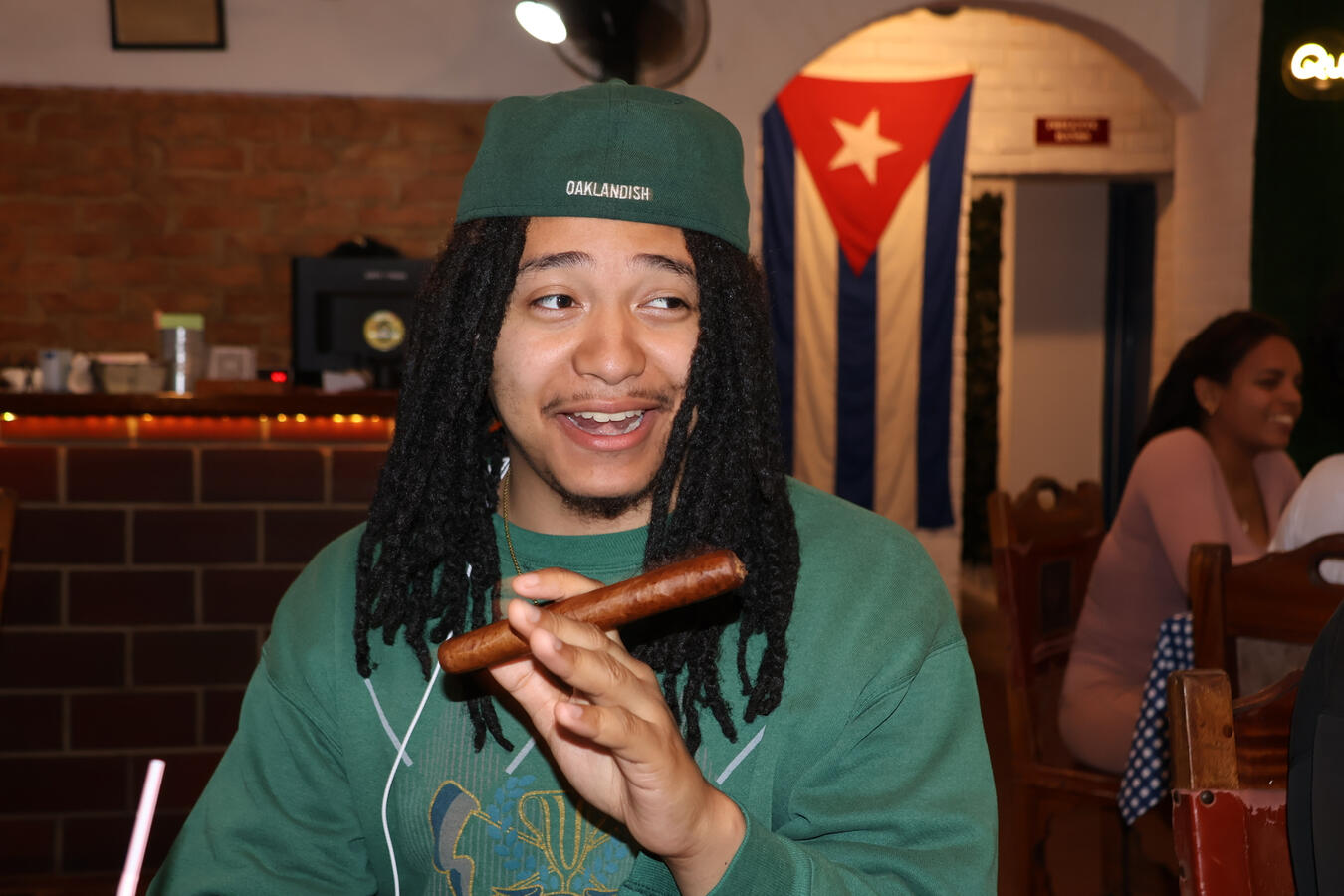 Fellow Enjoying a Cuban Evening Out A young delegation member holds a cigar inside a restaurant decorated with a Cuban flag.
