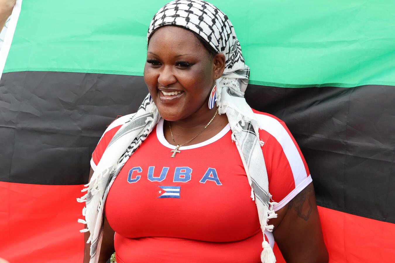 A woman wears a headscarf and Cuba's flag colors in front of a Pan-African flag backdrop.