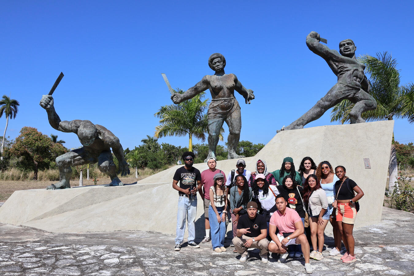 The delegation poses together in front of bronze statues at a monument in Cuba.