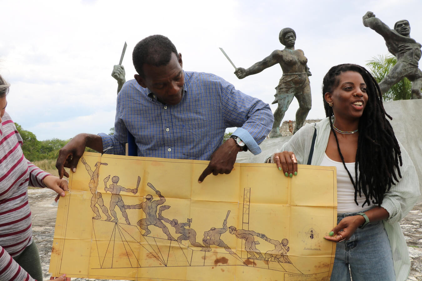 Two delegation members hold up a painting depicting a historical scene near a monument.