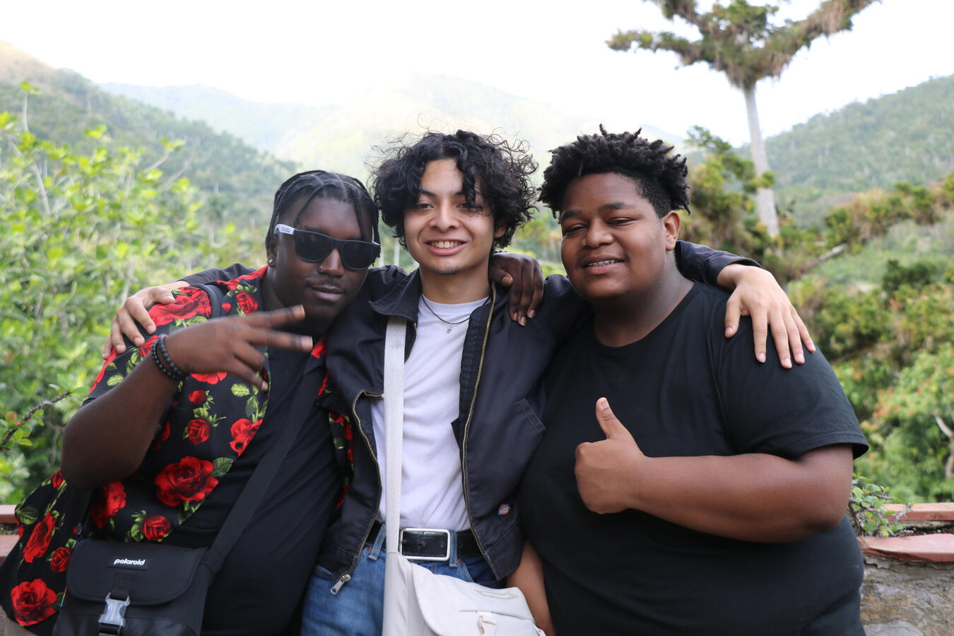 Three young delegation members pose closely together with hills in the background.