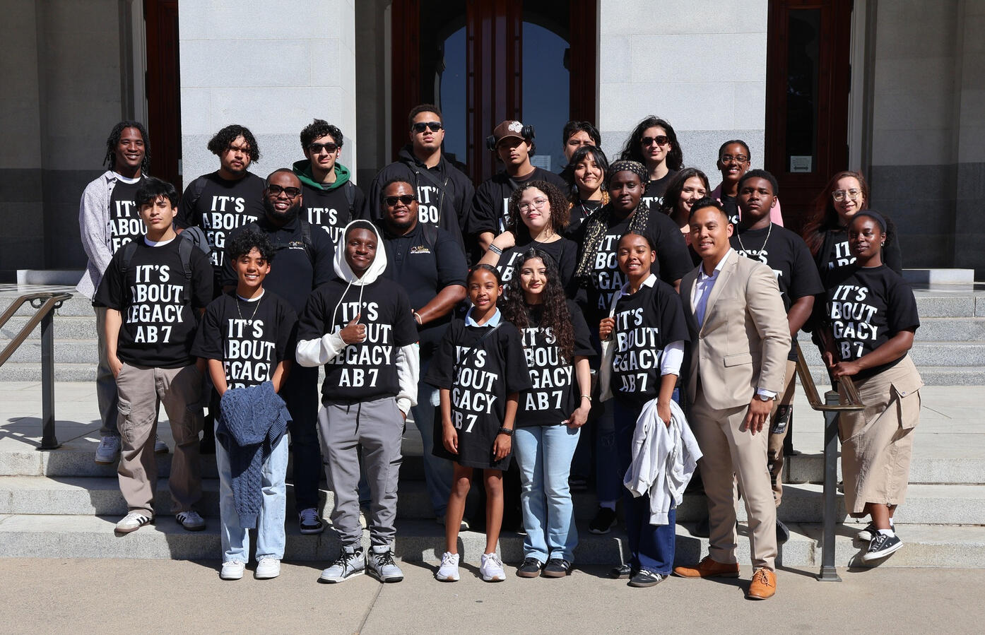 A group of advocates in Legacy campaign shirts poses on stone steps with a man in a suit.