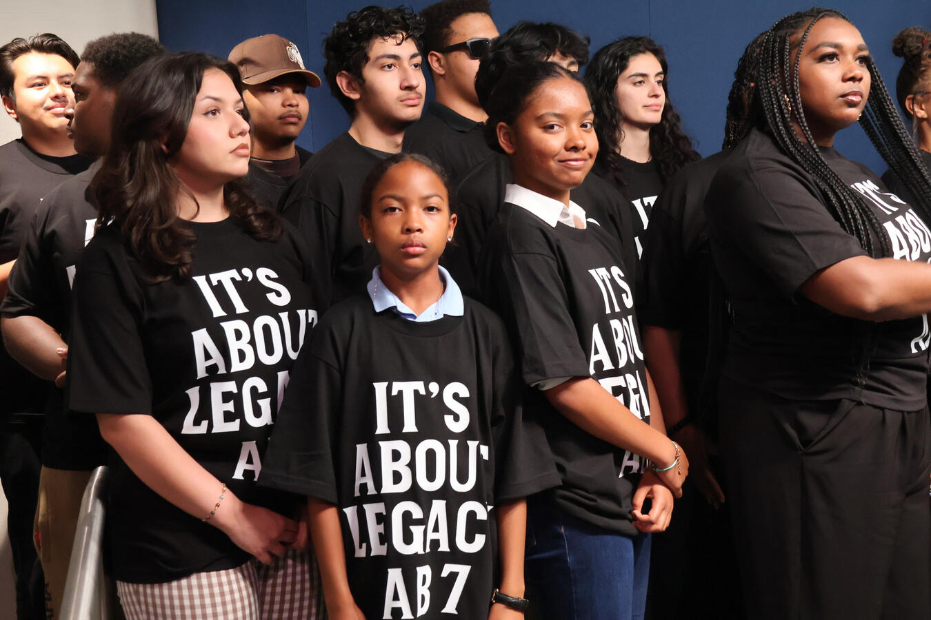 A row of young advocates wearing matching black shirts reading It's About Legacy, AB7.