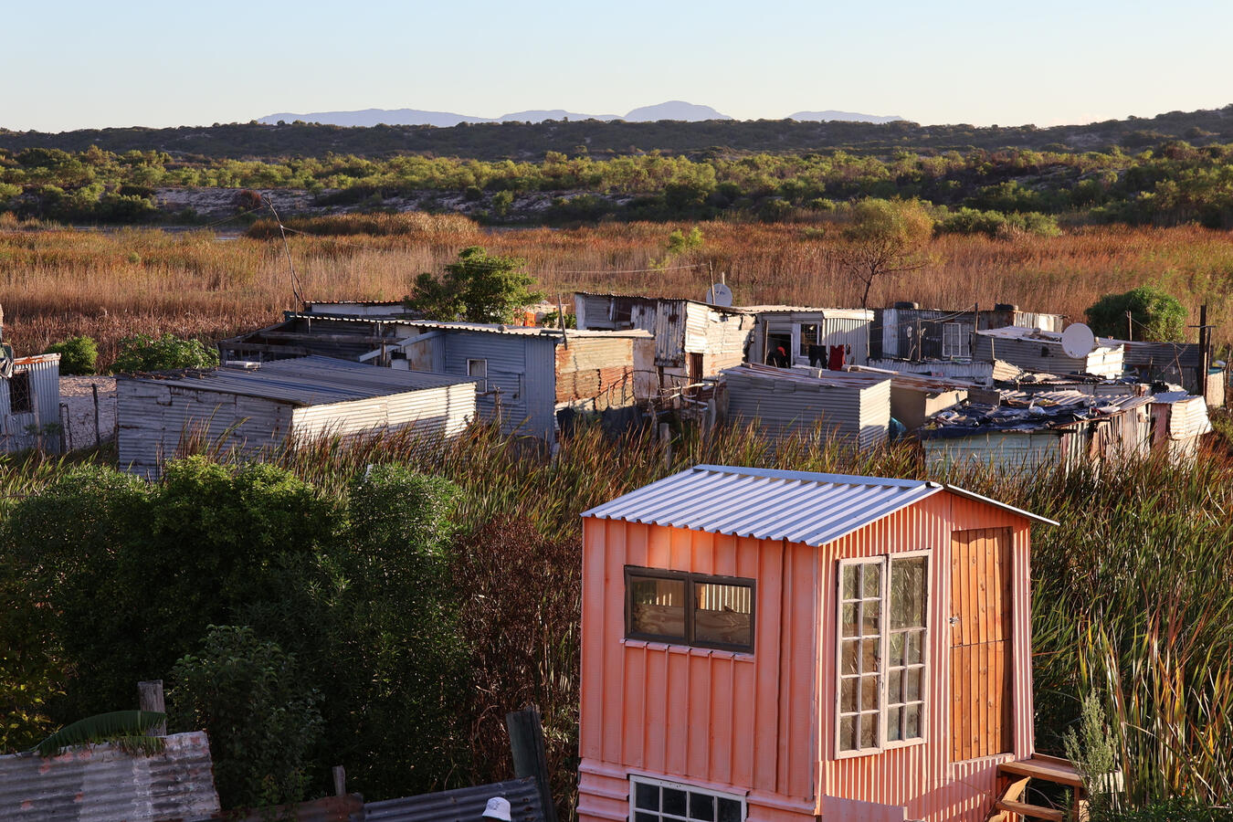 Small homes, including a brightly painted shed, sit along a dirt road in a Cape Town township.