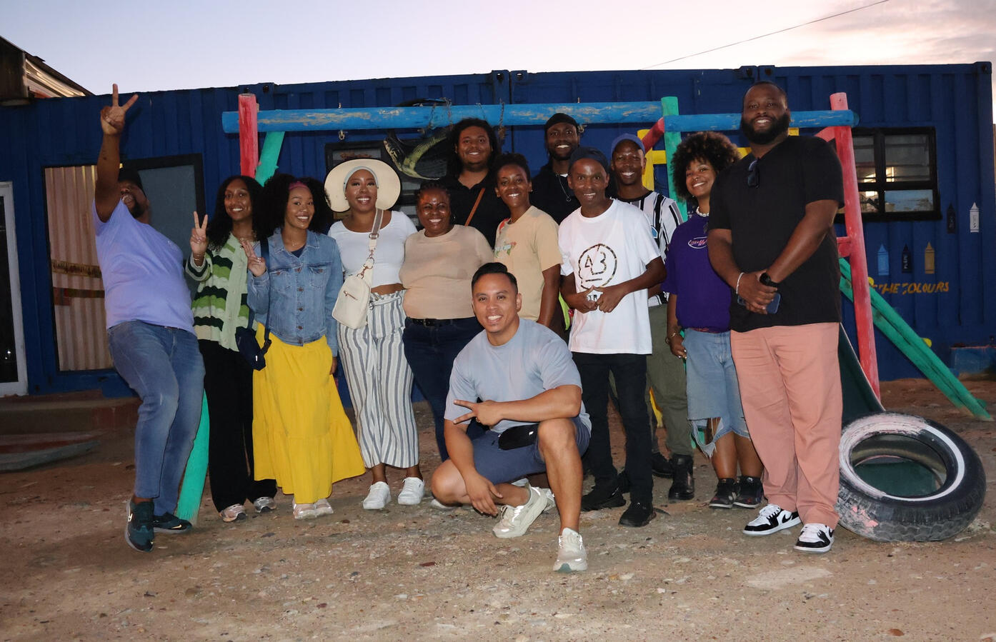 The delegation poses with local hosts outdoors in the evening, with colorful decorations behind them.