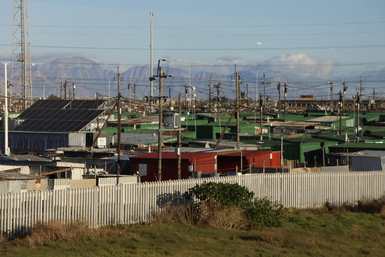A dense township of small homes stretches across a Cape Town hillside beneath a clear sky.